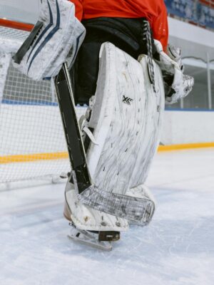 A hockey goalie in full gear stands on an indoor ice rink.