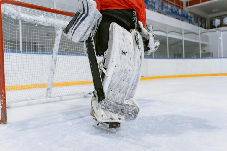 A hockey goalie in full gear stands on an indoor ice rink.