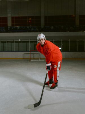 A male ice hockey player in red uniform posing on ice rink indoors.