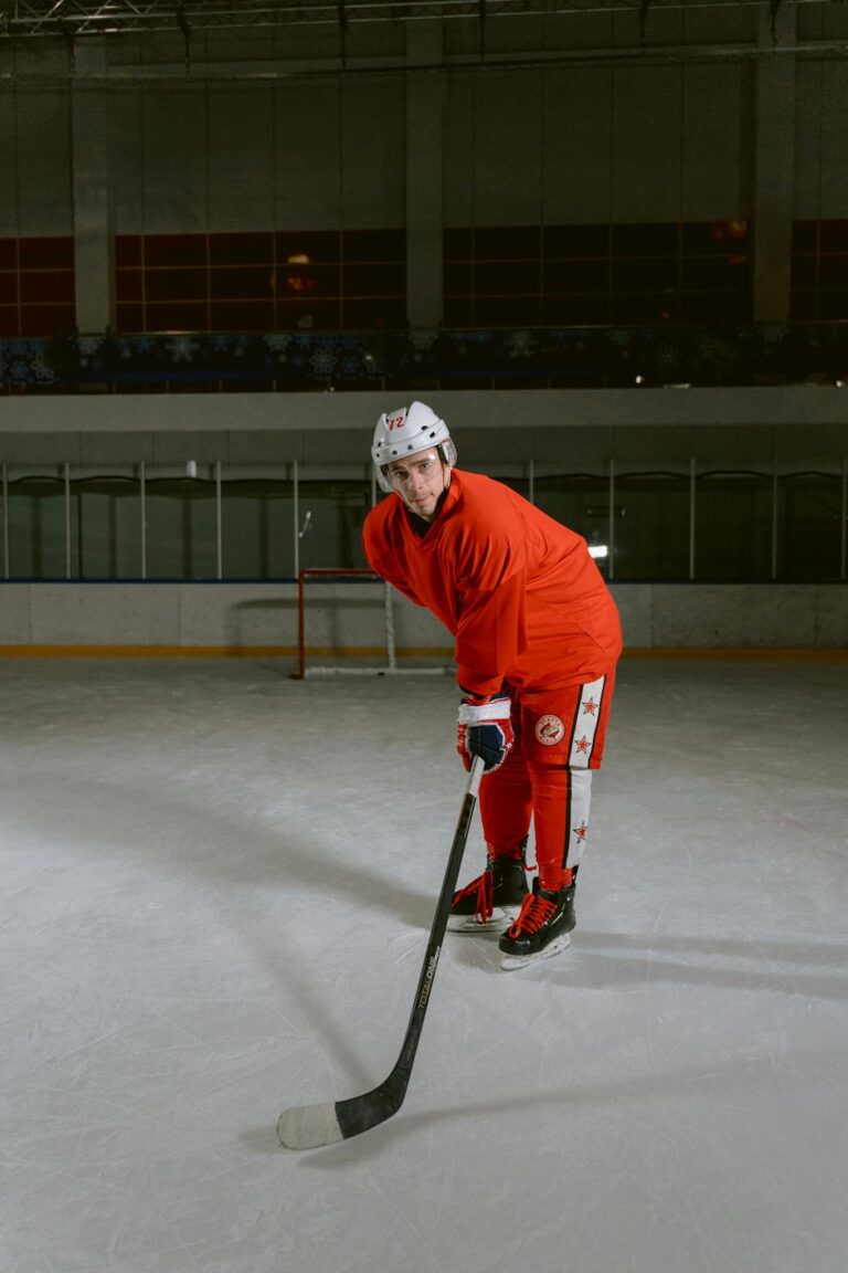 A male ice hockey player in red uniform posing on ice rink indoors.
