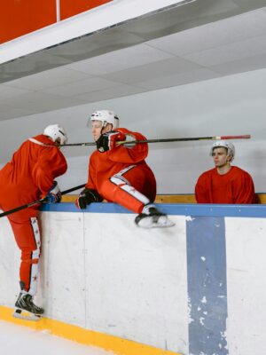Hockey players practicing indoors wearing red uniforms and white helmets on an ice rink.